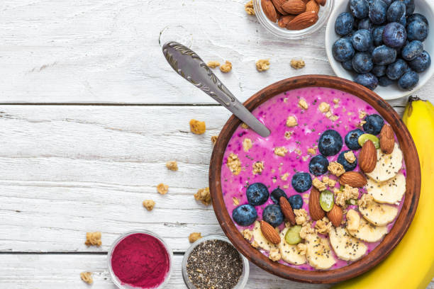 A pink smoothie bowl with banana, blueberries, almonds, and granola